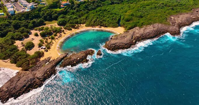 Turquoise water splashes on the rocky shore of Mar-Chiquita Beach in Puerto Rico. Iconic secluded beach surrounded by lush greenery.