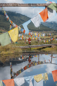 View of colorful prayer flags fluttering in the breeze above a reflective surface, with mountains in the distance, Phobjikha Valley, Wangdue Phodrang, Bhutan.