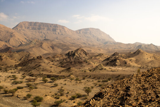 View of the rugged, arid landscape unfolds with rocky outcroppings and sparse vegetation under a hazy sky, Wadi Bani Khalid, Ash Sharqiyah North Governorate, Oman.