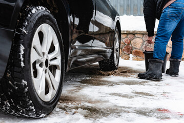 Obraz premium Man hand-washing black car using brush and bucket in winter.