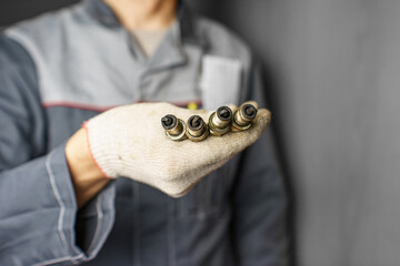 A mechanic holds old spark plugs. Defective spark plugs, stained with motor oil. Soot on the spark plugs.