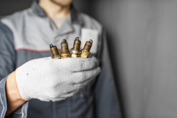 A mechanic holds old spark plugs. Defective spark plugs, stained with motor oil. Soot on the spark plugs.