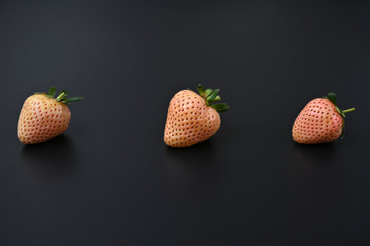 three fresh pineberries on a black background