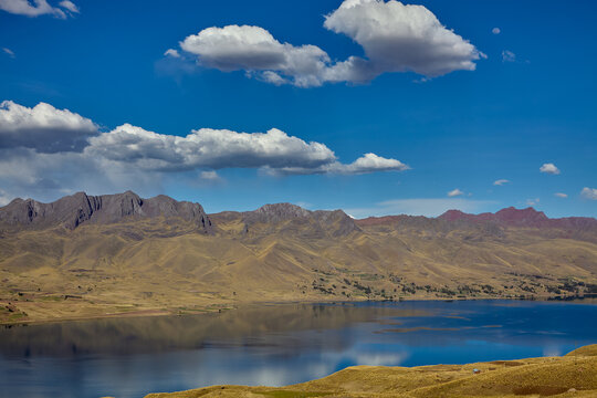 Langui Layo lagoon, located in the province of Canas near Espinar, Cusco, featuring deep blue waters reflecting a bright sky and white clouds. The surrounding Andean landscape 