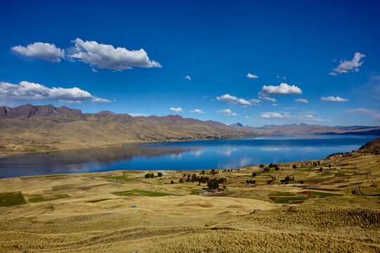 Langui Layo lagoon, located in the province of Canas near Espinar, Cusco, featuring deep blue waters reflecting a bright sky and white clouds. The surrounding Andean landscape 