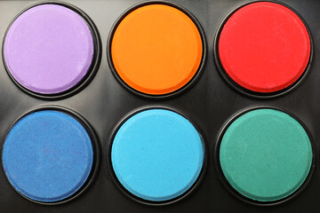 Palette with watercolor paints as background, top view