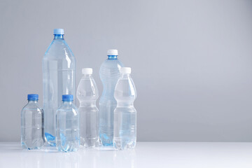 Naklejka premium Water bottles of different sizes on white table against grey background, space for text