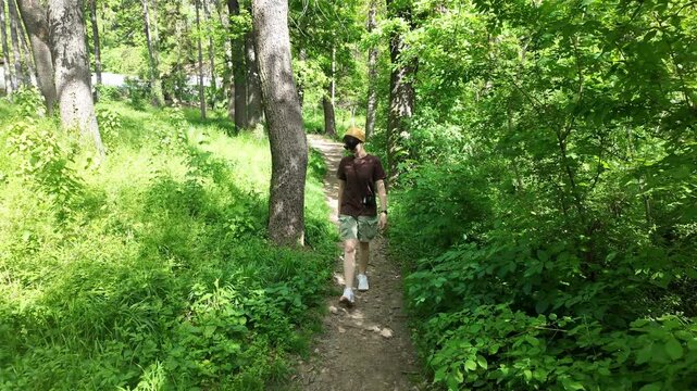 Young woman walking along a narrow forest path surrounded by green trees and sunlight. Concept of outdoor lifestyle, nature connection, calm movement and mindful walking