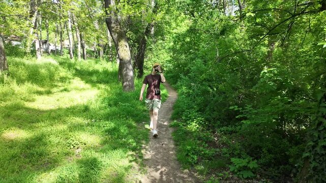 Young woman walking along a narrow forest path surrounded by green trees and sunlight. Concept of outdoor lifestyle, nature connection, calm movement and mindful walking