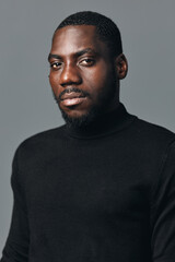 Obraz premium African man portrait with beard wearing black turtleneck sweater in creative conceptual visual style studio. Serious expression, dark skin, closeup with soft lighting on gray background.