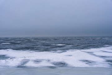 Minimalist scene: frozen water surface covered in thin ice and snow extending to the distant horizon veiled by fog