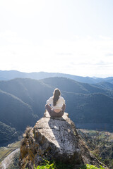 woman meditating on cliff overlooking mountains, practicing sunrise mindfulness during solo nature retreat, serene sunlight, panoramic