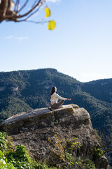 woman meditating on cliff overlooking mountains, practicing sunrise mindfulness during solo nature retreat, serene sunlight, panoramic
