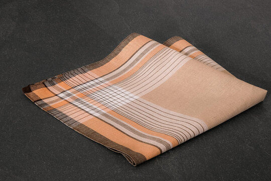 Neatly folded beige handkerchief with a classic orange and brown striped pattern, displayed on a dark, textured stone surface.
