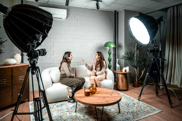 Two women having conversation during a video recording session, cameras and lighting equipment setup in a professional studio