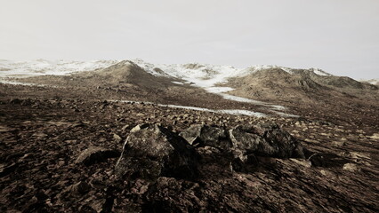 Vast and rugged terrain stretches across the view, with scattered rocks and sparse vegetation. Snow dusted mountains loom in the distance, creating a striking contrast against the earth tones.