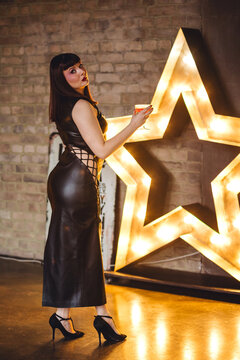 Sexy elegant beautiful gorgeous self confident plus size middle age woman in the leather black dress celebrating with a fancy cocktail. Body positive concept. Self sufficient happy life without man