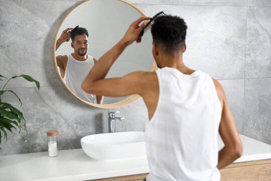 Handsome man combing his hair near mirror in bathroom