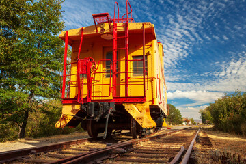 A Caboose On A Blue Sky Day sitting on the tracks with a train station in the distance
