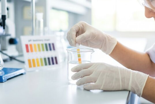 Scientist tests water sample in laboratory with pH strip showing different colors for analysis and results