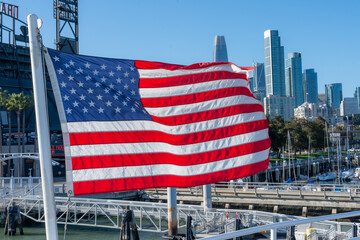 American flag waving against the backdrop of San Francisco cityscape. Patriotic symbol of the United States with an urban skyline, representing freedom, national pride, and American culture