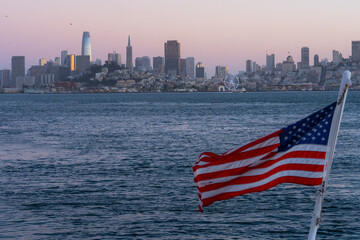 American flag waving against the backdrop of San Francisco cityscape. Patriotic symbol of the United States with an urban skyline, representing freedom, national pride, and American culture