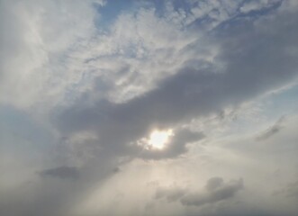 Obraz premium Bright sun shining through dramatic clouds in a soft blue sky, hope and nature concept