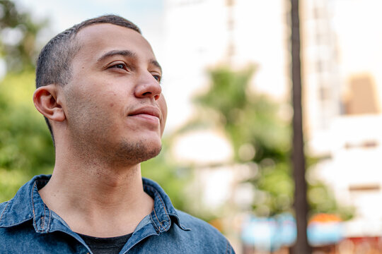 Thoughtful young man in a denim shirt looking into the distance outdoors in a city park