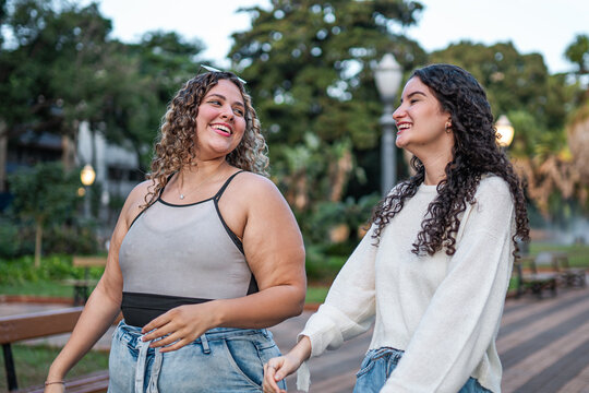 Two happy young female friends walking and laughing together in a city park