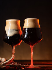 Two beers in stylish glasses. Craft beer porter or stout . Foam overflows from the glass