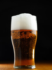 Close-up of a light foamy beer glass on the table. Black background