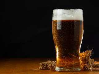 Cold beer glass in drops of water on a wooden table with a black background