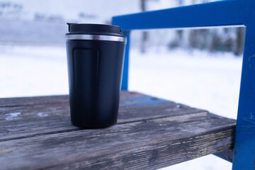 Obraz premium Hot drink cup sits on wooden table in snow-covered outdoor area during winter time
