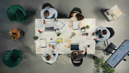 Top down view of work team in multinational company analyzing metrics and projections. Staff collaborates on strategy planning and report sharing to support business targets. © DC Studio