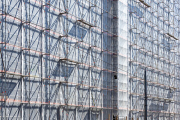 Metal Scaffolding Grid on Building Facade with White Protective Mesh Sheeting for Urban Construction and Renovation Projects