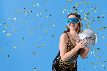 Naklejka premium Young woman in carnival mask with disco ball and confetti on blue background