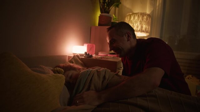 Loving and caring father covering his daughter with soft blanket and switching off light in her room