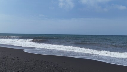 Peaceful Black Sand Beach with Gentle Ocean Waves and Clear Blue Sky