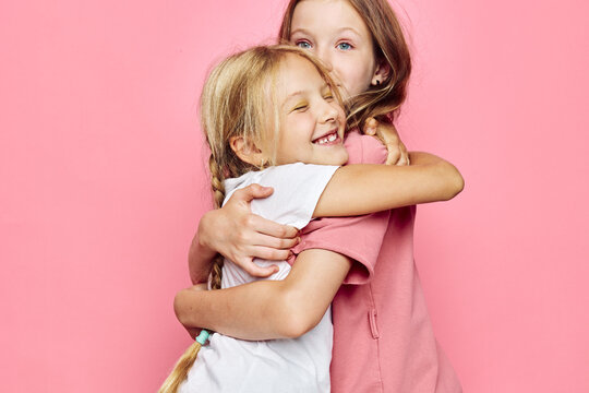 Two happy girls hugging each other against pink background. Smiling siblings show affection and warmth. Concept of friendship, love, and family bond.