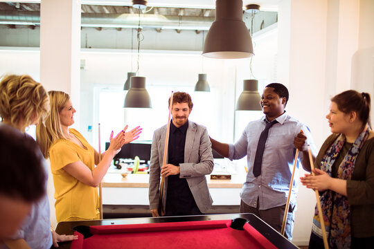 Coworkers celebrating around a pool table in modern office