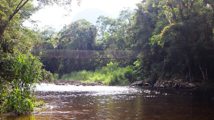 Obraz premium The suspension bridge over the Marumbi River, located in Morretes, Paraná, Brazil, features crystal-clear waters, rapids, and stunning natural landscapes at the foot of the Serra do Marumbi mountain 