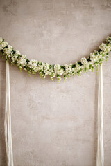 Obraz premium Thai flower garland phuangmalai hanging on textured wall with white jasmine and green leaves creating traditional decorative arrangement for celebration or ceremony