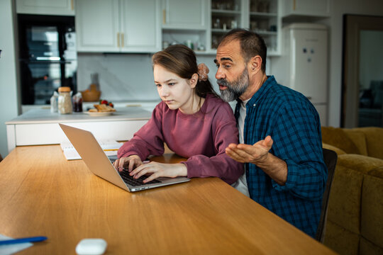Parent helping teenage girl with laptop homework at kitchen table