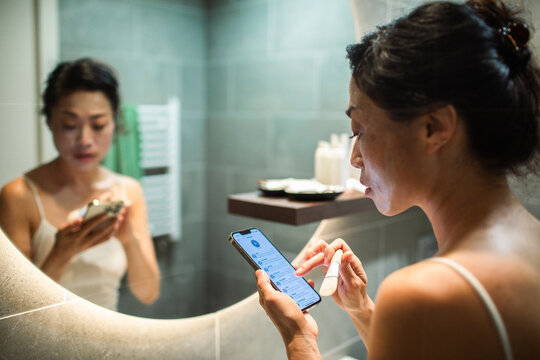Woman using smartphone during skincare routine in bathroom