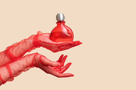 Female hands in red lace gloves with bottle of perfume on beige background