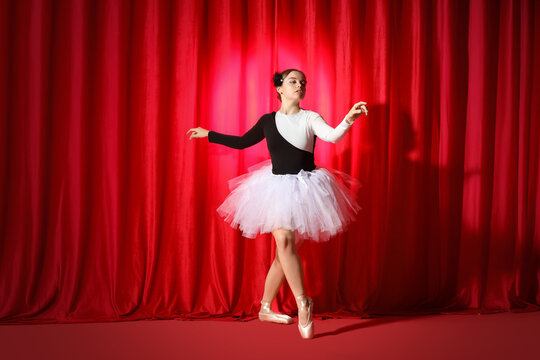 Young ballerina dancing near red curtains