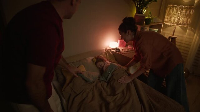 Handheld shot of mother and father adjusting blanket while their little daughter sleeping peacefully and mother switching off light