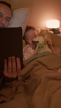 Vertical shot of Caucasian parents chatting with daughter and enjoying watching cartoon in bed