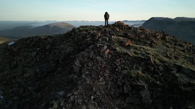 Glen Coe, Scottish Highlands - aerial over the mountains in winter with hill walker standing on summit of mountain - reveal of glen and Rannoch Moor