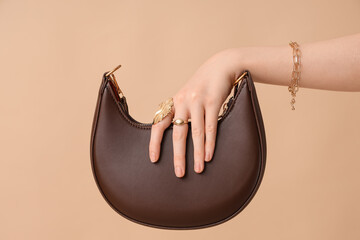 Female hand in beautiful golden bracelet and rings with stylish bag on brown background
